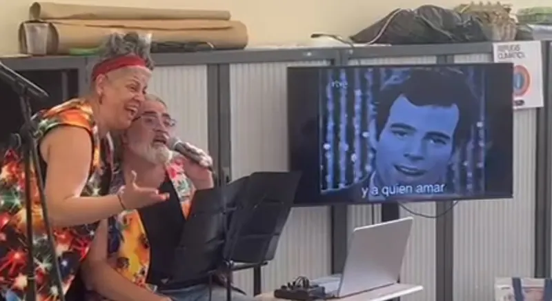 Angie y Albert ríen mientras cantan; en la pantalla, la letra «y a quién amar».